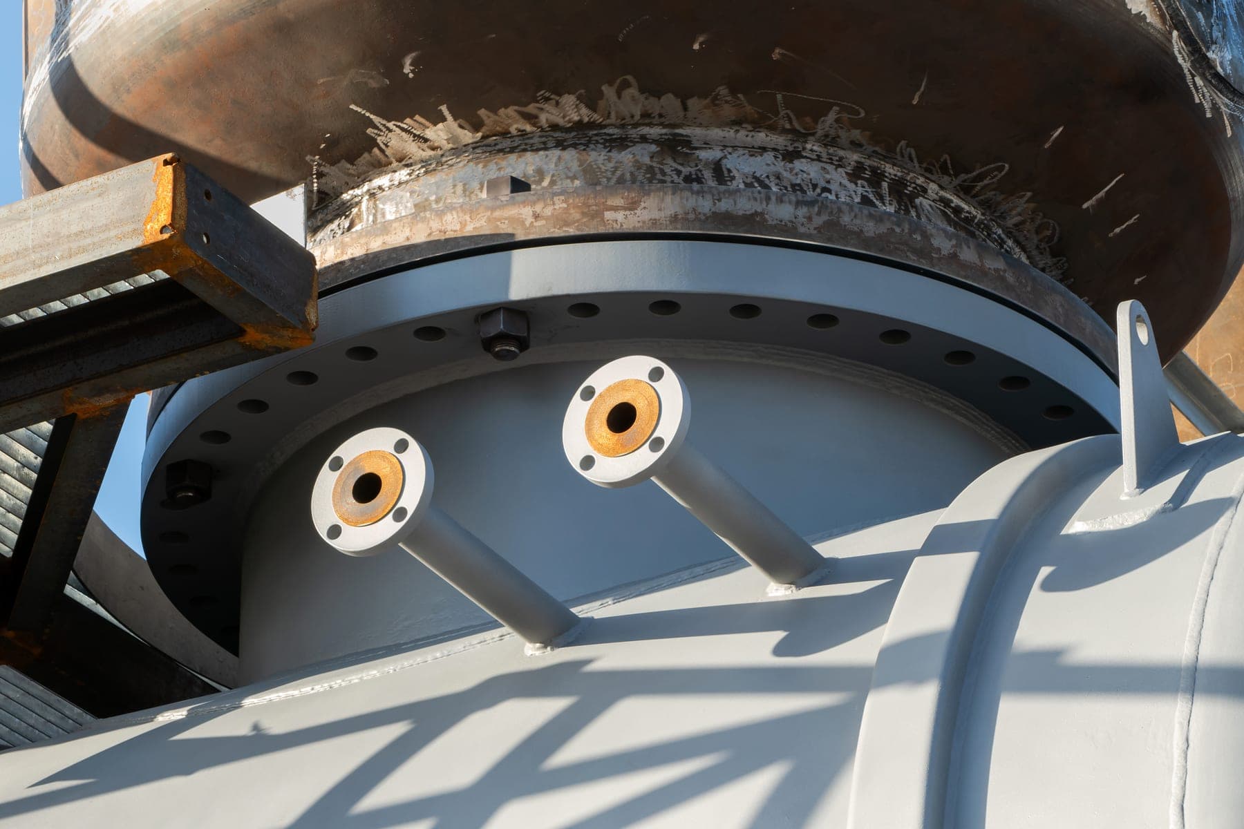 Close-up of flanged pipe couplings on the head of a large pressure vessel.
